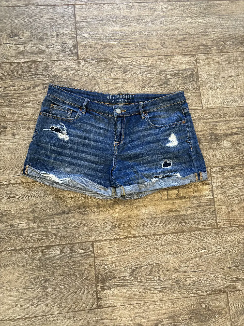 Short de jean de mujer, tiro medio, con detalles de roturas y dobladillo en el borde. Ideal para un look casual y moderno.