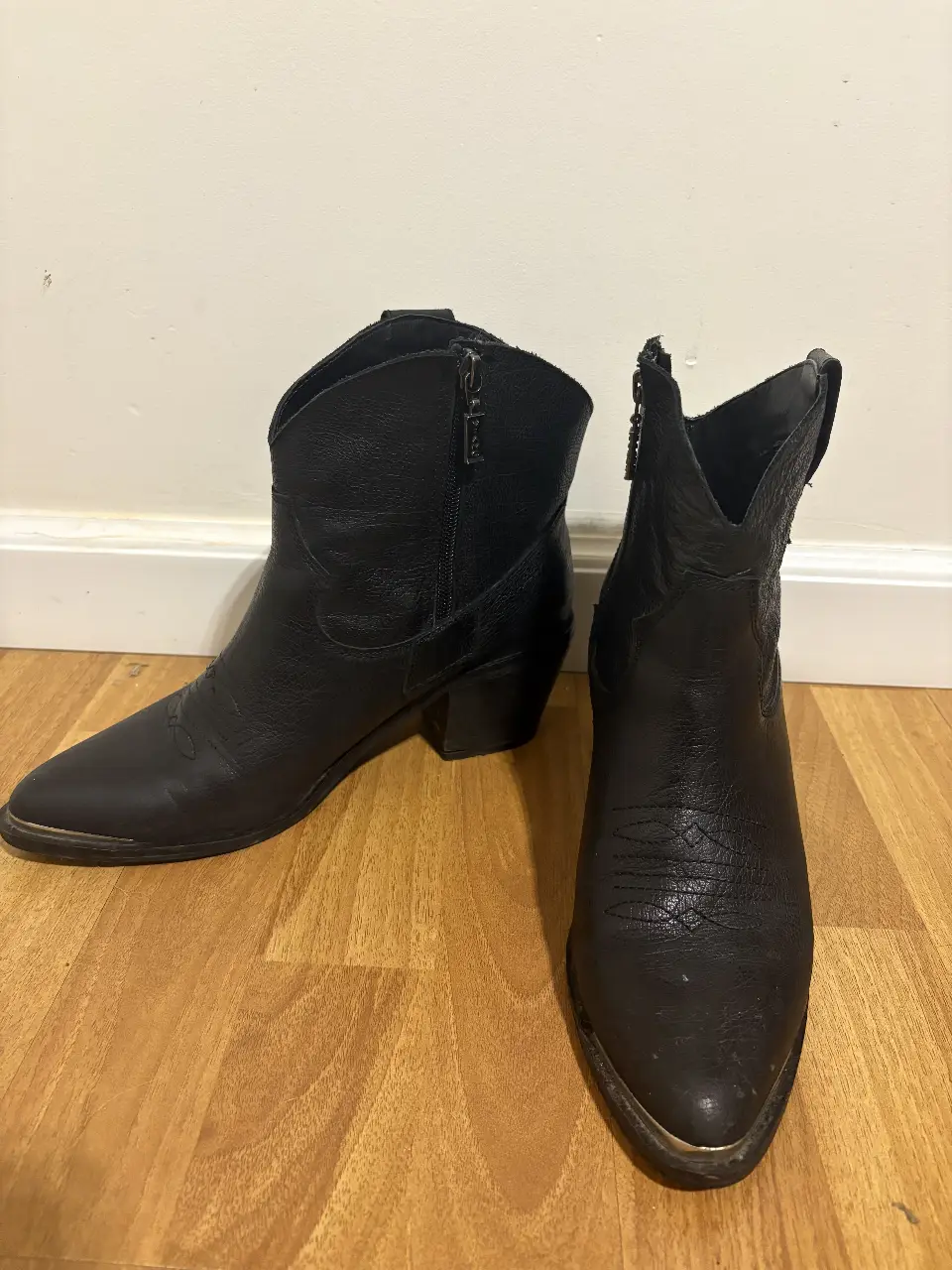 Botines de cuero negro con cierre lateral y detalles dorados en la suela. Estilo cowboy, ideales para un look casual y moderno.