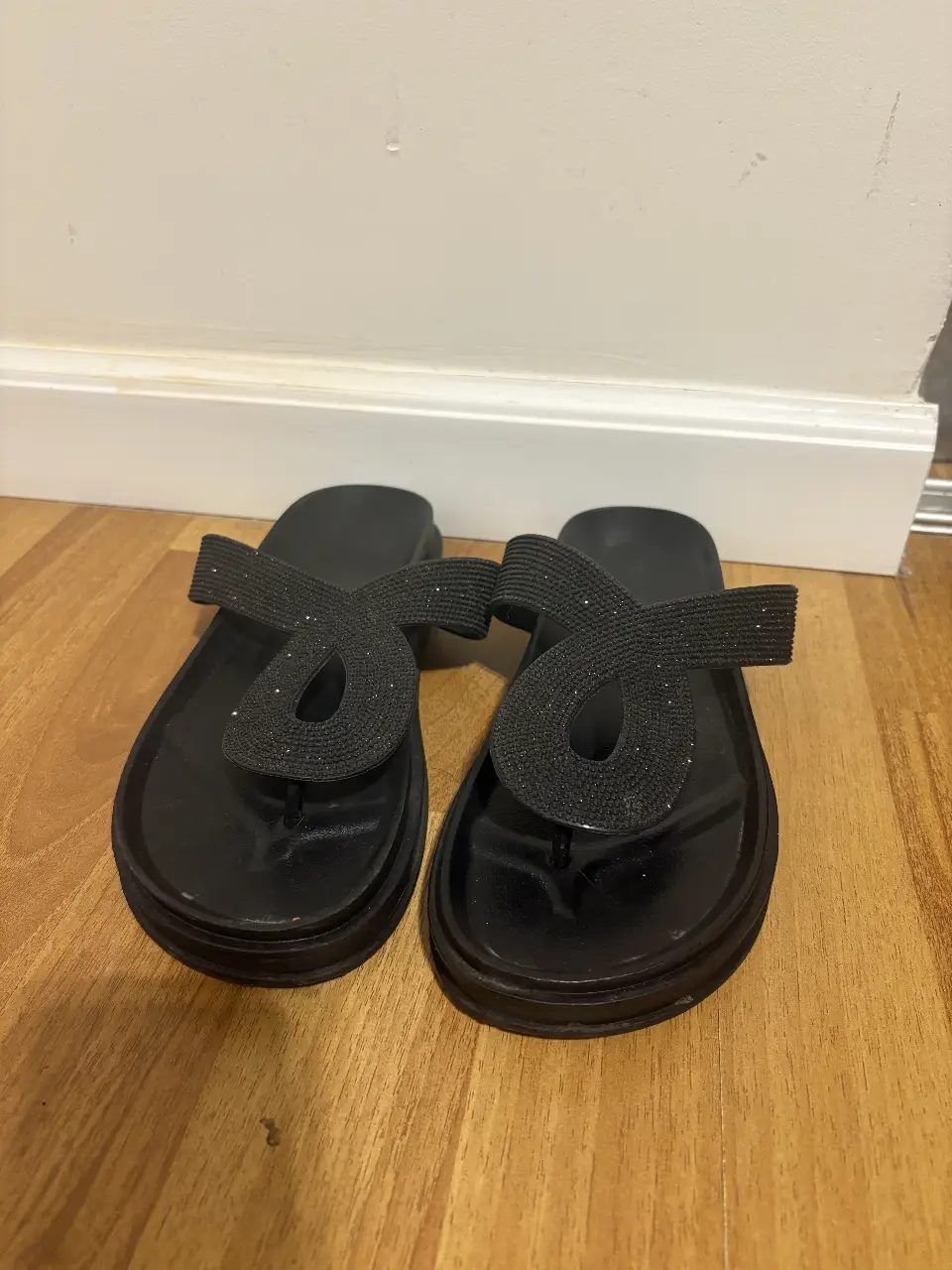 Sandalias de dedo negras con detalle de diseño en la tira superior. Ideales para un look casual y cómodo.