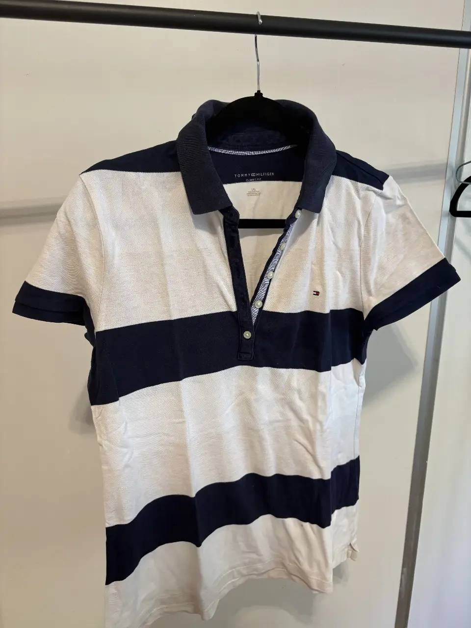 Remera polo Tommy Hilfiger a rayas horizontales en blanco y azul marino. Corte clásico, con cuello y mangas en azul. Ideal para un look casual y deportivo.