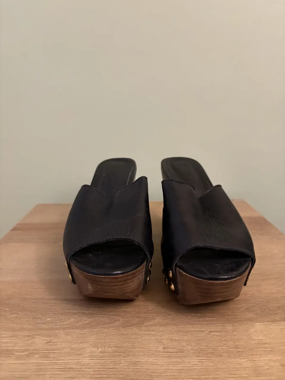 Sandalias de cuero negro con plataforma de madera y detalles dorados. Ideales para un look moderno y sofisticado.