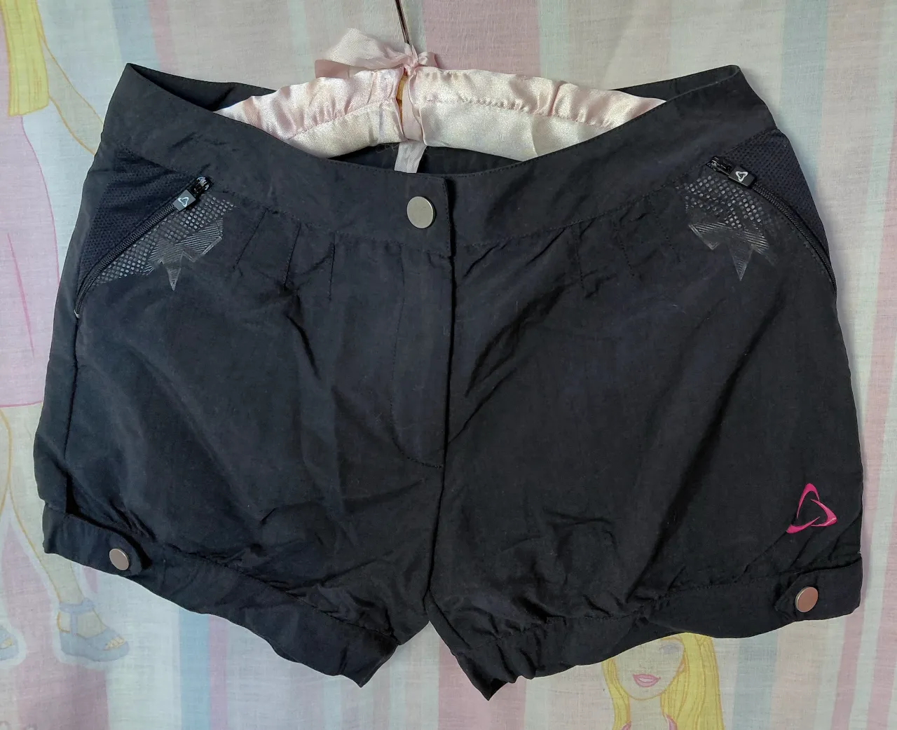 Short deportivo negro con detalles en rosa y bolsillos con cierre. Ideal para actividades al aire libre.