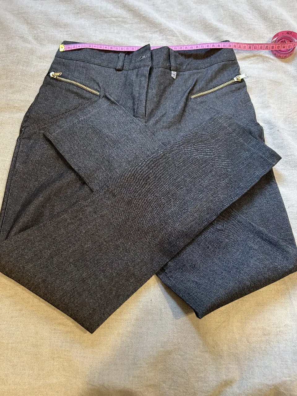 Pantalón sastrero de mujer, color gris oscuro. Con detalles de cierre dorado en los bolsillos delanteros. Ideal para un look elegante y moderno.