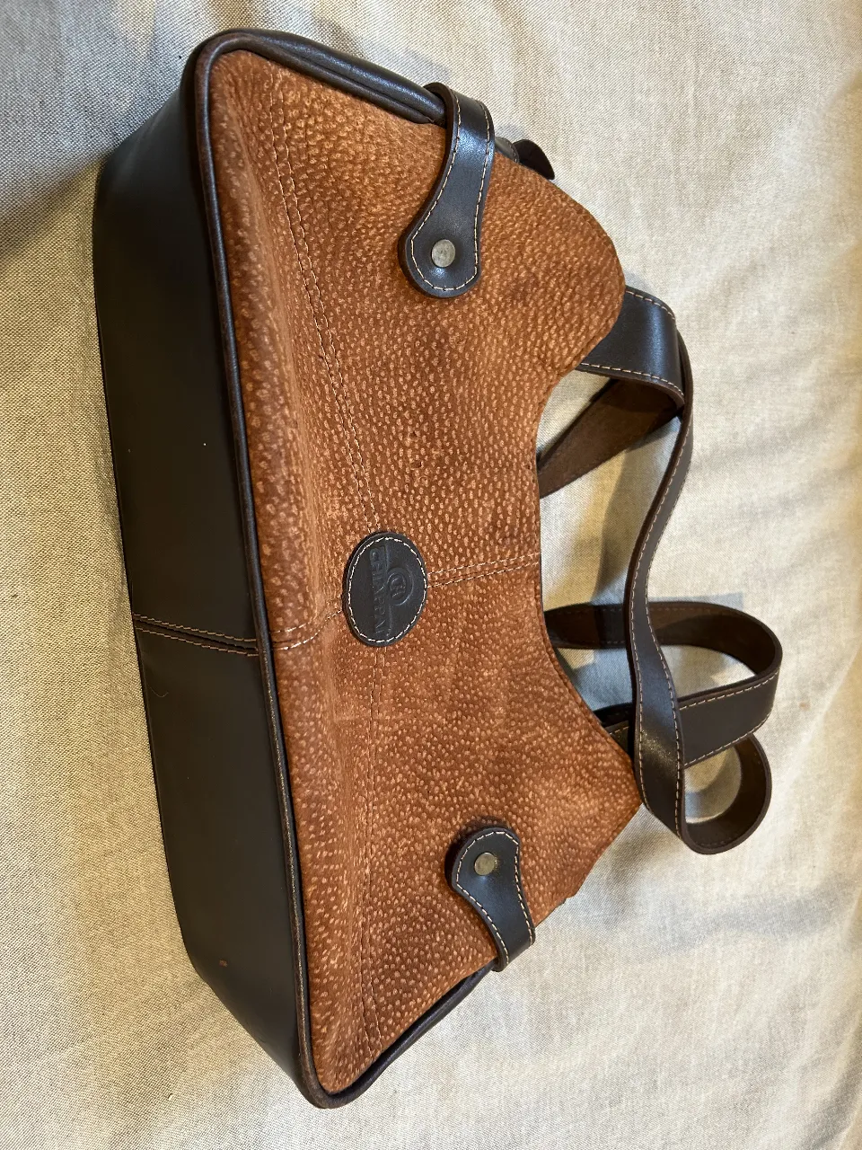 Cartera de hombro de cuero marrón con textura. Detalles en cuero oscuro y logo de la marca. Interior espacioso con múltiples compartimentos.