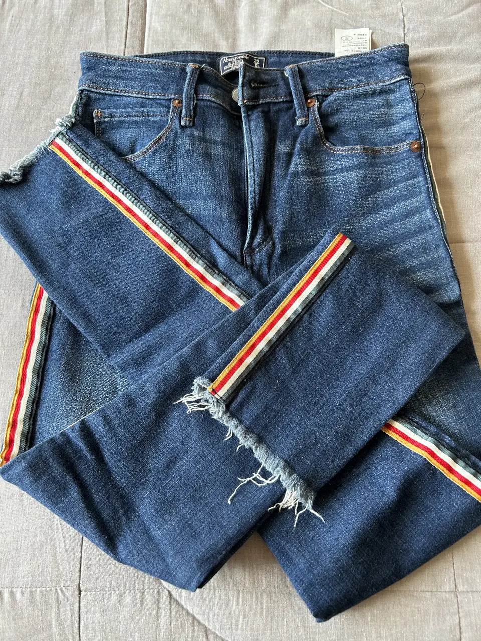 Jeans rectos de mujer, tiro medio, con detalles de rayas en los laterales en colores rojo, blanco y amarillo. Un clásico renovado para un look casual y moderno.