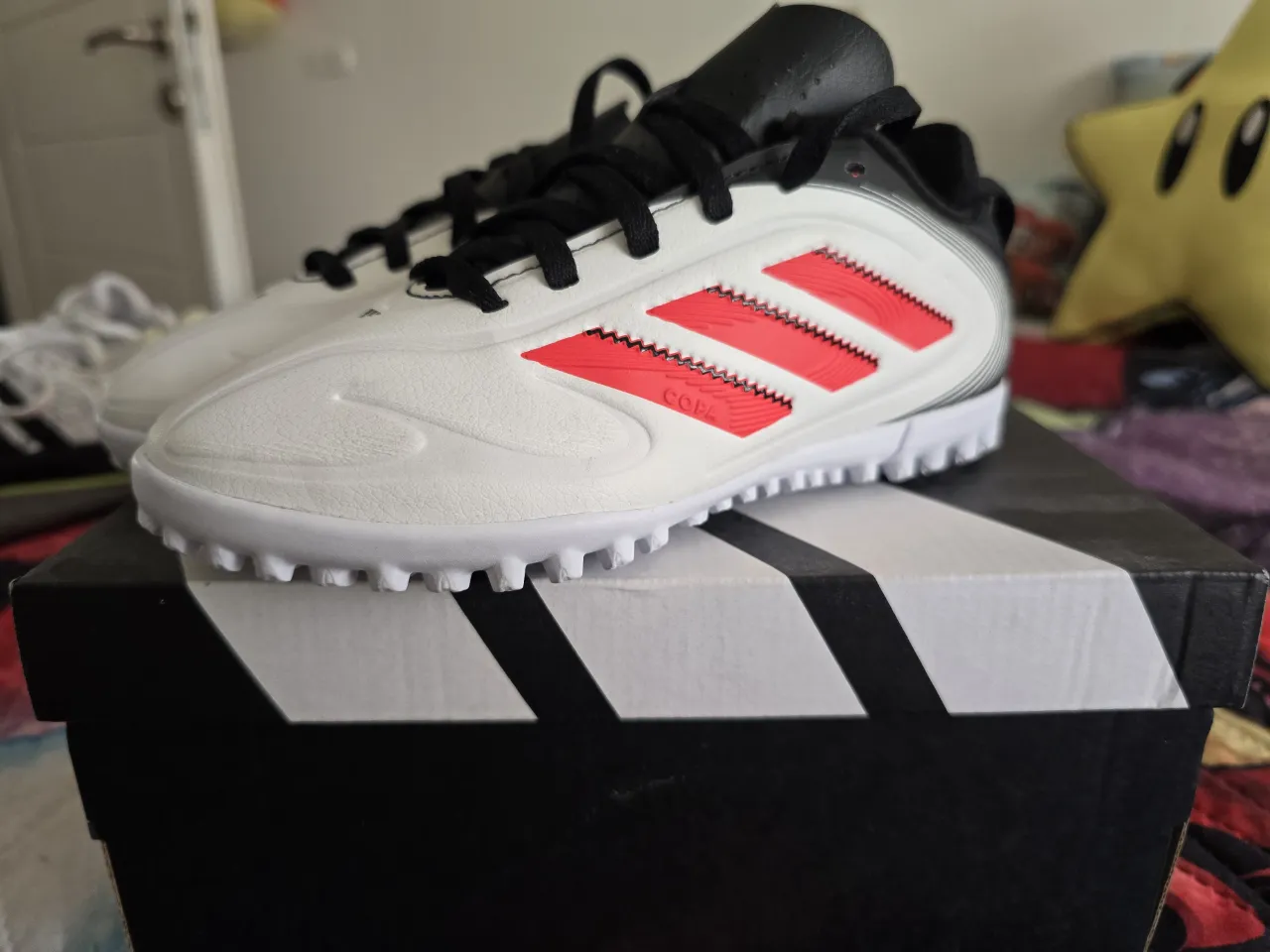 Botines de fútbol para césped sintético, color blanco con detalles en rojo y negro. Marca Adidas.