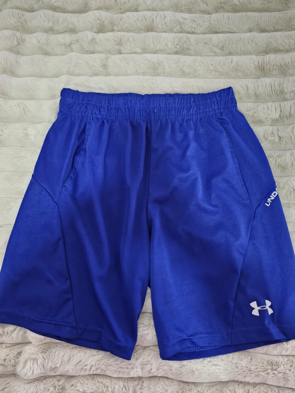 Short deportivo azul de hombre, con logo de Under Armour en blanco. Ideal para entrenamientos y actividades físicas.