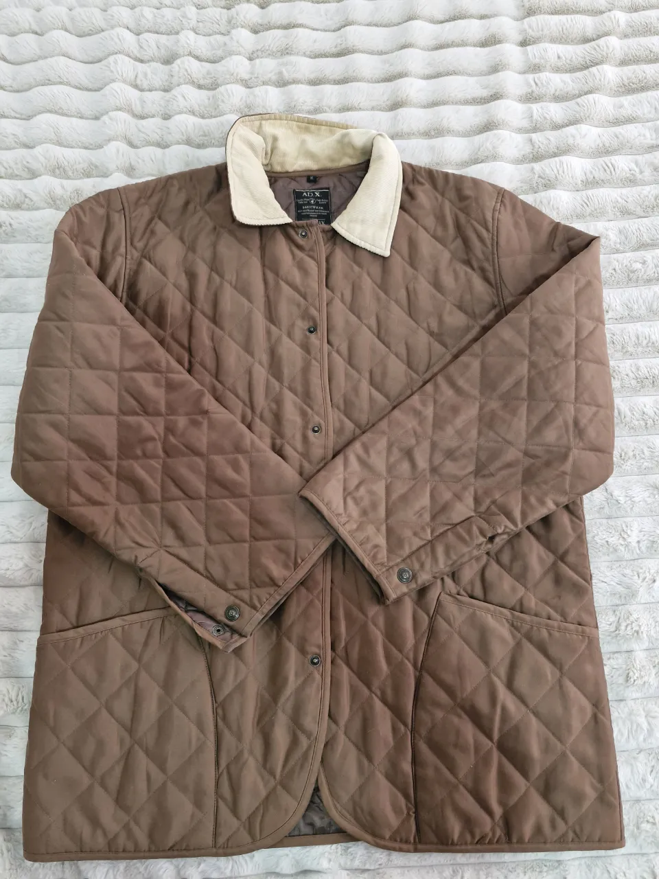 Campera ADX acolchada marrón con cuello de pana beige. Ideal para el invierno, estilo casual y utilitario. Posee dos bolsillos frontales y cierre con botones.