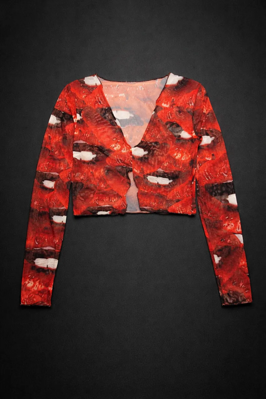 Top Mesh "Red Lips"
Diseño: Estampado integral de labios en tonos rojo, negro y blanco.
Corte: Silueta cropped con escote en "V" pronunciado.
Tela: Mesh de viscosa/poliéster con spandex; liviana, elástica, suave al tacto y con una transparencia sutil muy sastrera. Estilo grunge/moderno.