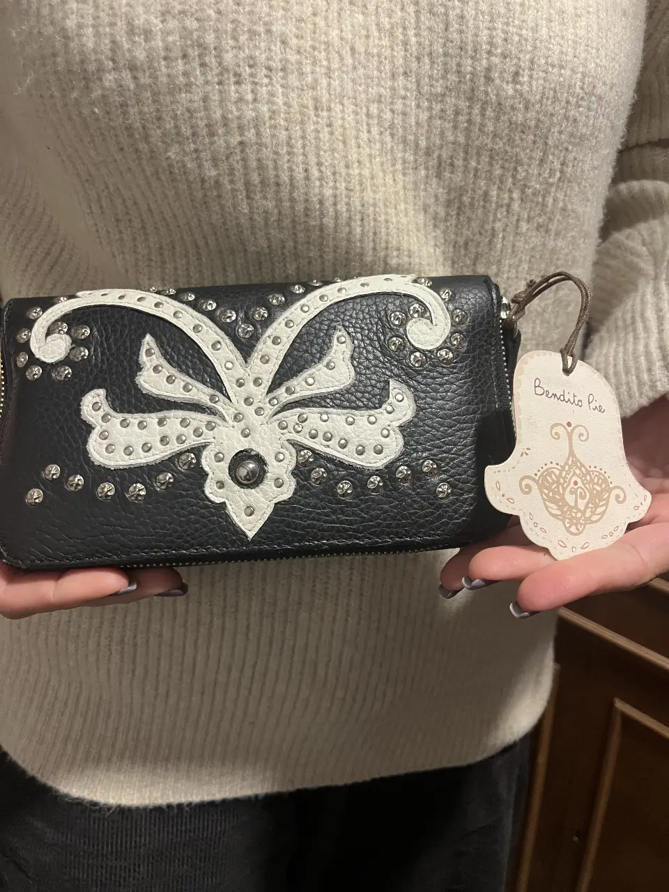 Billetera negra de cuero con detalles en blanco y tachas. Diseño con solapa y cierre, ideal para llevar tus esenciales con estilo.