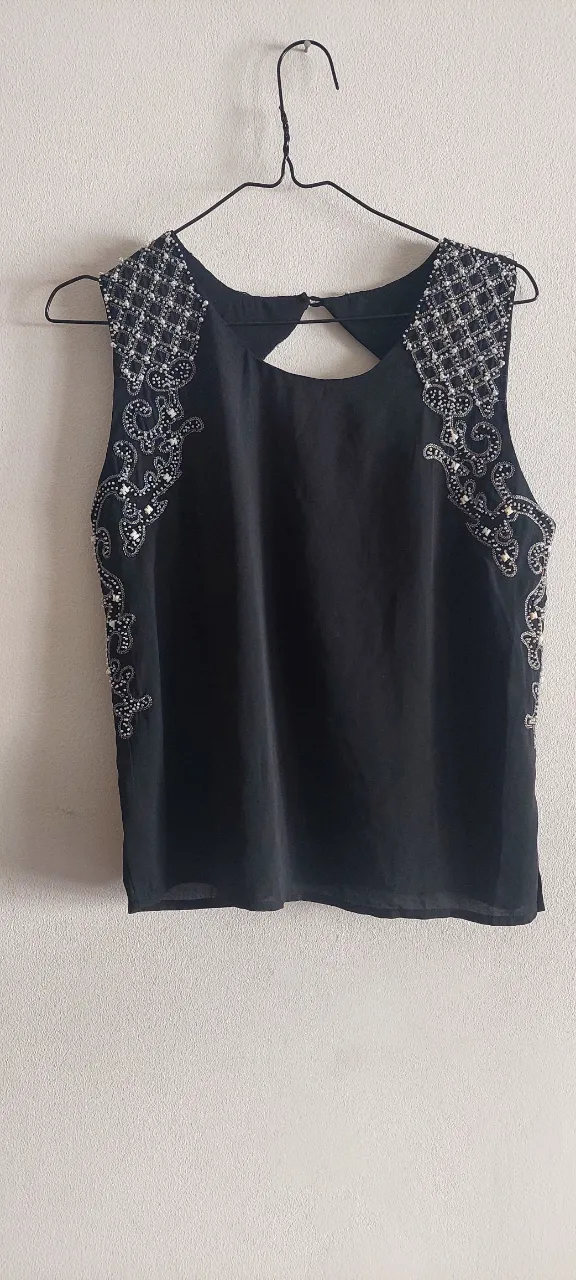 Top negro con detalles bordados y pedrería en hombros y cuello. Posee un corte en la espalda.