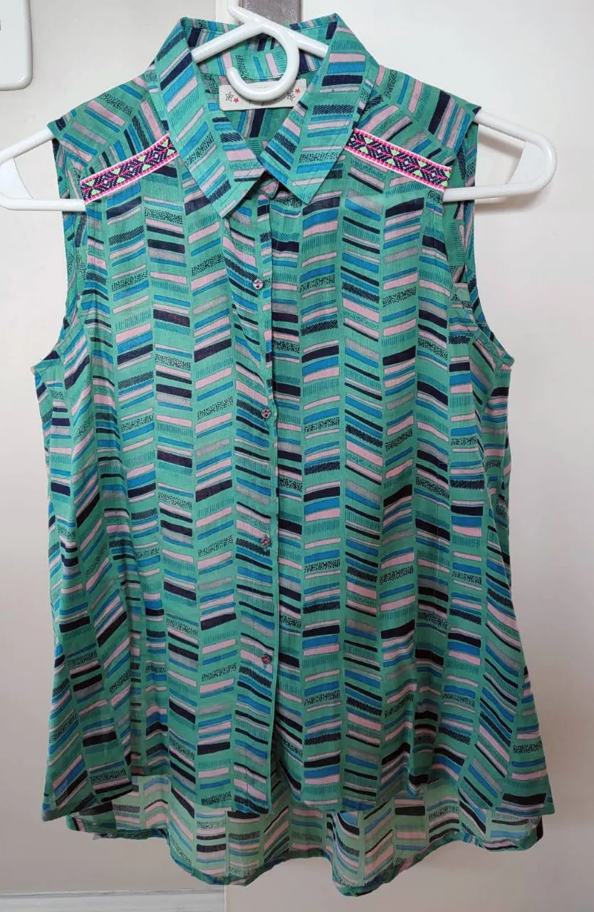 Blusa sin mangas con estampado geométrico en tonos verdes y azules. Detalles bordados en los hombros y cuello camisero. Ideal para un look fresco y casual.