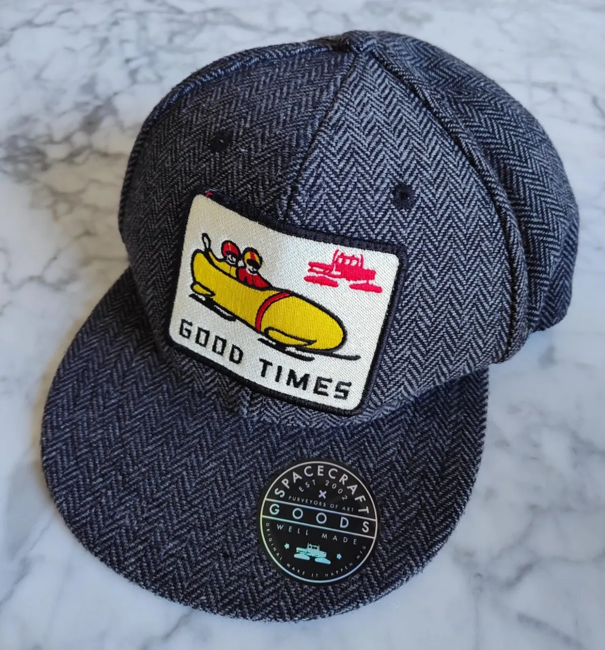 Gorra Spacecraft Goods con diseño de bobsleigh y la frase "Good Times". Confeccionada en tejido de espiga gris, visera curva y ajuste trasero. Un accesorio de estilo casual y urbano.