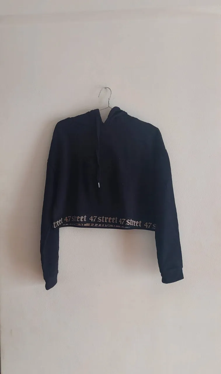 Remera crop top negra con capucha y estampa "47 street" en la cintura. Ideal para un look urbano y canchero.