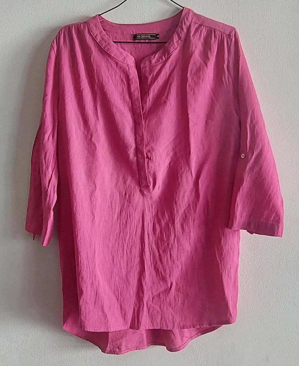 Remera manga 3/4 de color rosa vibrante, ideal para un look casual y fresco. Posee un cuello mao con una pequeña abertura y botones, y un detalle de puños enrollados con botón. Perfecta para combinar con jeans o pantalones claros.