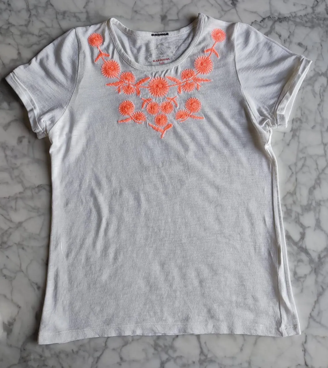 Remera blanca de mujer con bordado floral en el cuello. Ideal para un look casual y fresco.