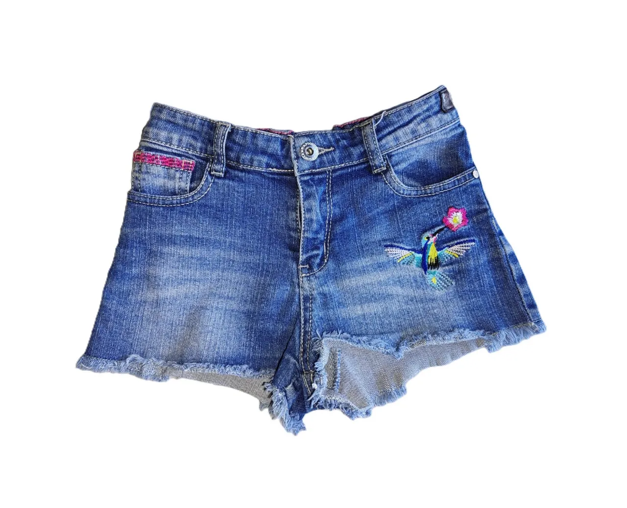 Short de jean de niña con bordado de flores y colibrí. Tiro medio, con detalles de desgaste y flecos en el borde. Ideal para un look casual y fresco.