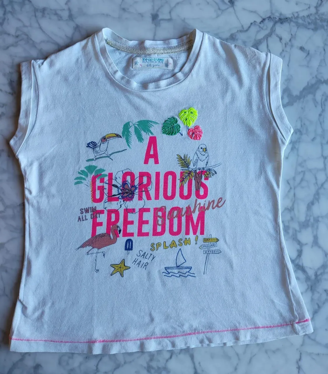 Remera sin mangas blanca con estampado de diseño tropical y la frase 'A Glorious Freedom'. Ideal para un look casual y fresco.