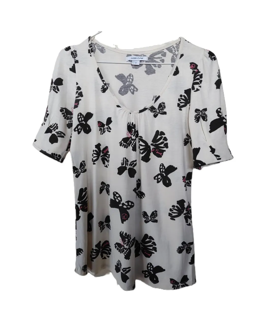 Remera de mujer con estampado de mariposas en blanco y negro. Cuello en V, mangas cortas con detalle de botones. Ideal para un look casual y femenino.