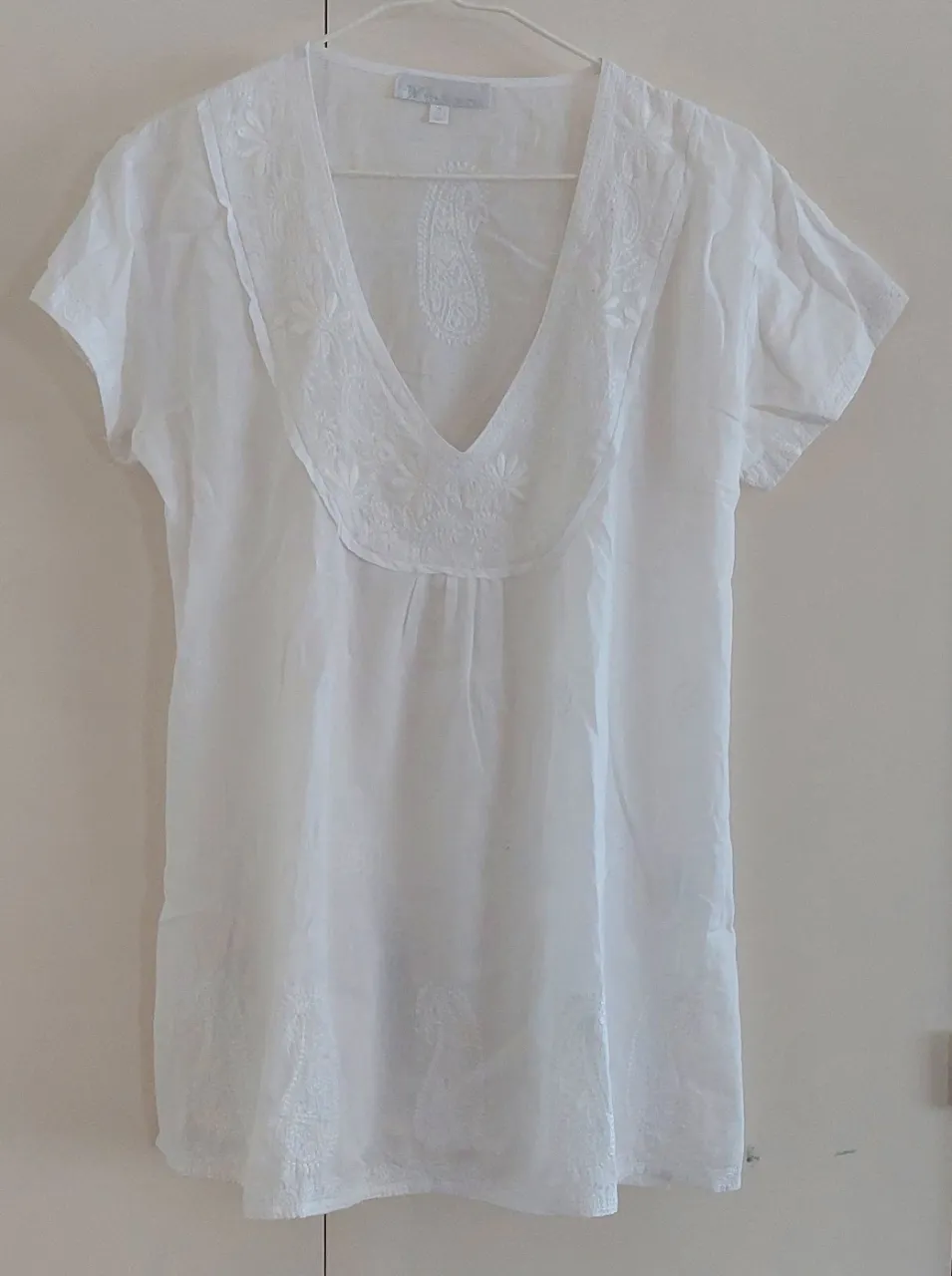 Blusa blanca con detalles bordados en el cuello y en la parte inferior. Diseño con escote en V y mangas cortas. Ideal para un look fresco y casual.