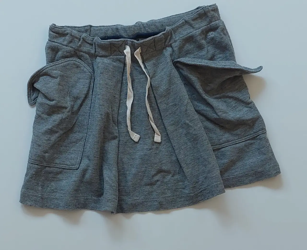 Short de tela de algodón gris, con bolsillos amplios y cintura elastizada con cordón. Ideal para un look casual y cómodo.