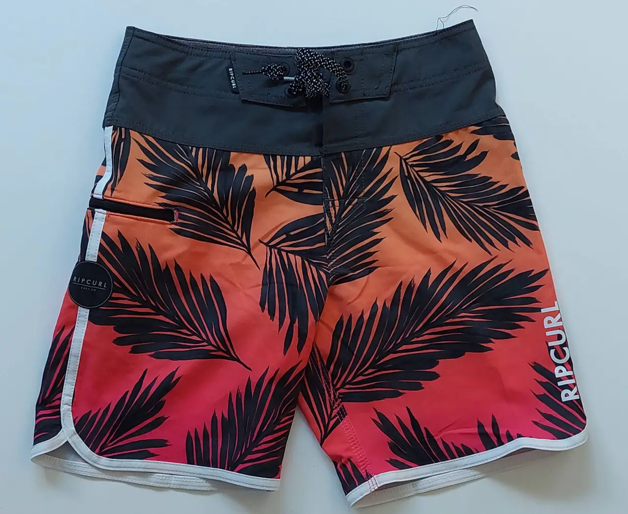 Short de baño Rip Curl Mirage con estampado de hojas tropicales en degradé naranja y rojo. Detalles en blanco y bolsillo con cierre. Talle 24.