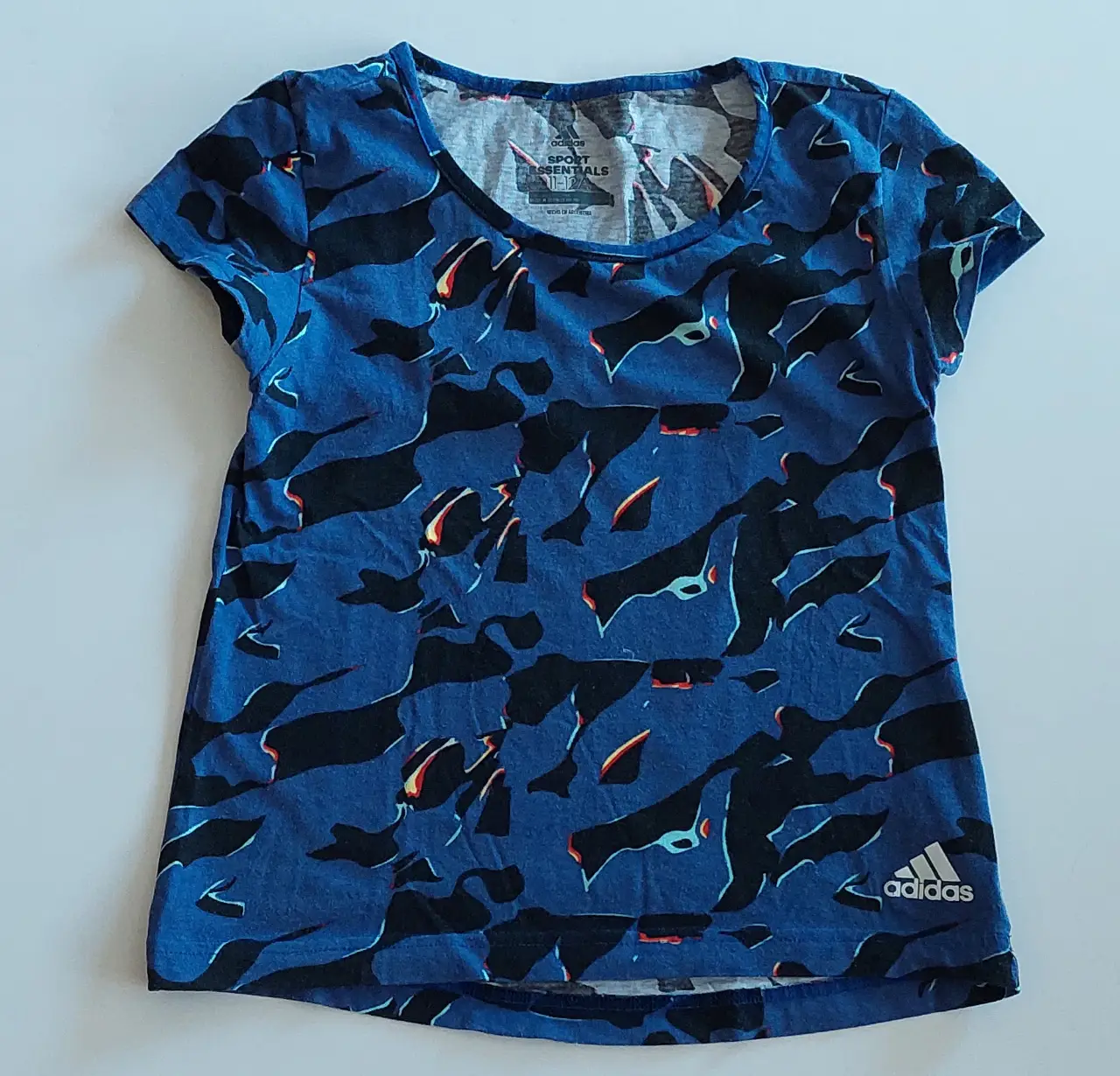 Remera deportiva Adidas Sport Essentials para niña, con estampado abstracto en tonos azules y negros. Ideal para actividades físicas.