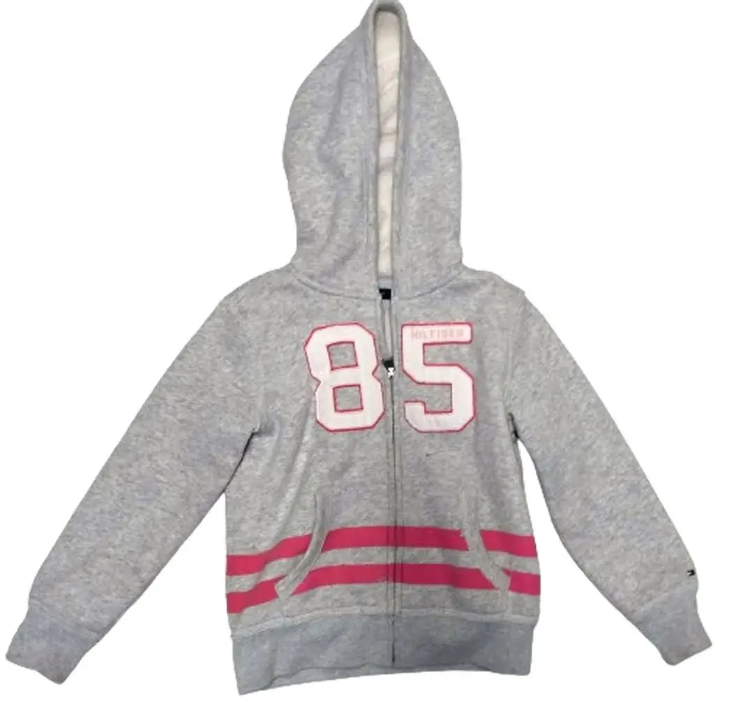 Buzo con cierre Tommy Hilfiger para niña, gris con detalles en rosa. Con el número 85 en el frente y rayas rosas en la parte inferior. Ideal para un look casual y abrigado.