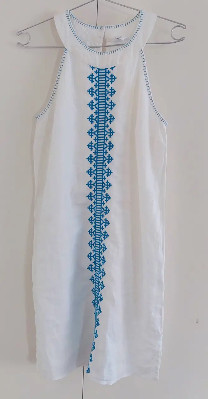 Vestido midi blanco forrado con detalles bordados en azul. Diseño halter con bordado central y detalles en el cuello y sisas. Ideal para un look fresco y casual.