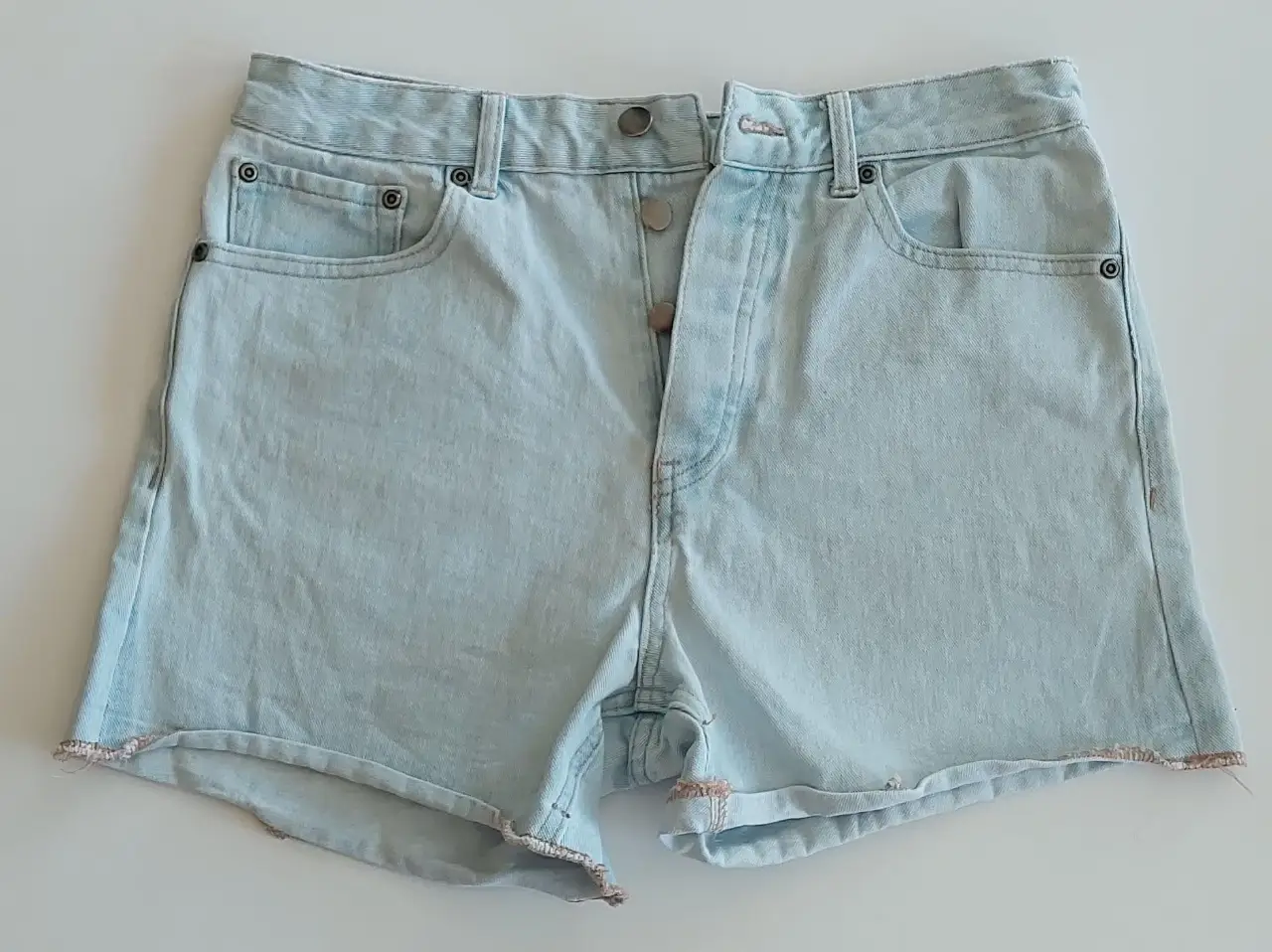 Short de jean celeste claro, tiro alto, con detalles de botones y bordes deshilachados. Ideal para un look casual y fresco.