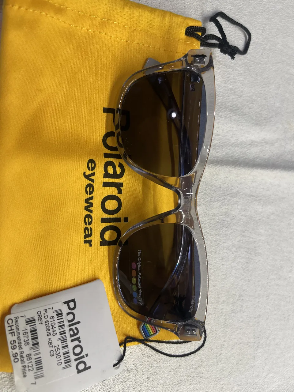 Anteojos de sol Polaroid, con marco transparente y lentes oscuros. Incluye estuche y etiqueta con precio recomendado.