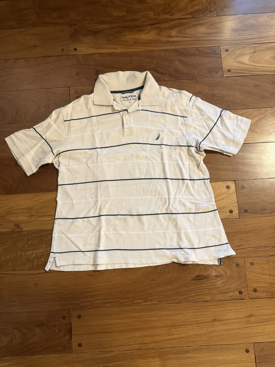 Remera polo clásica de manga corta, color beige con rayas finas horizontales en blanco y azul marino. Ideal para un look casual y cómodo.