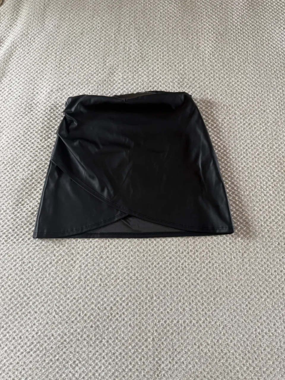 Pollera negra de cuero sintético, con un diseño cruzado y corte asimétrico. elastico en la cintura .