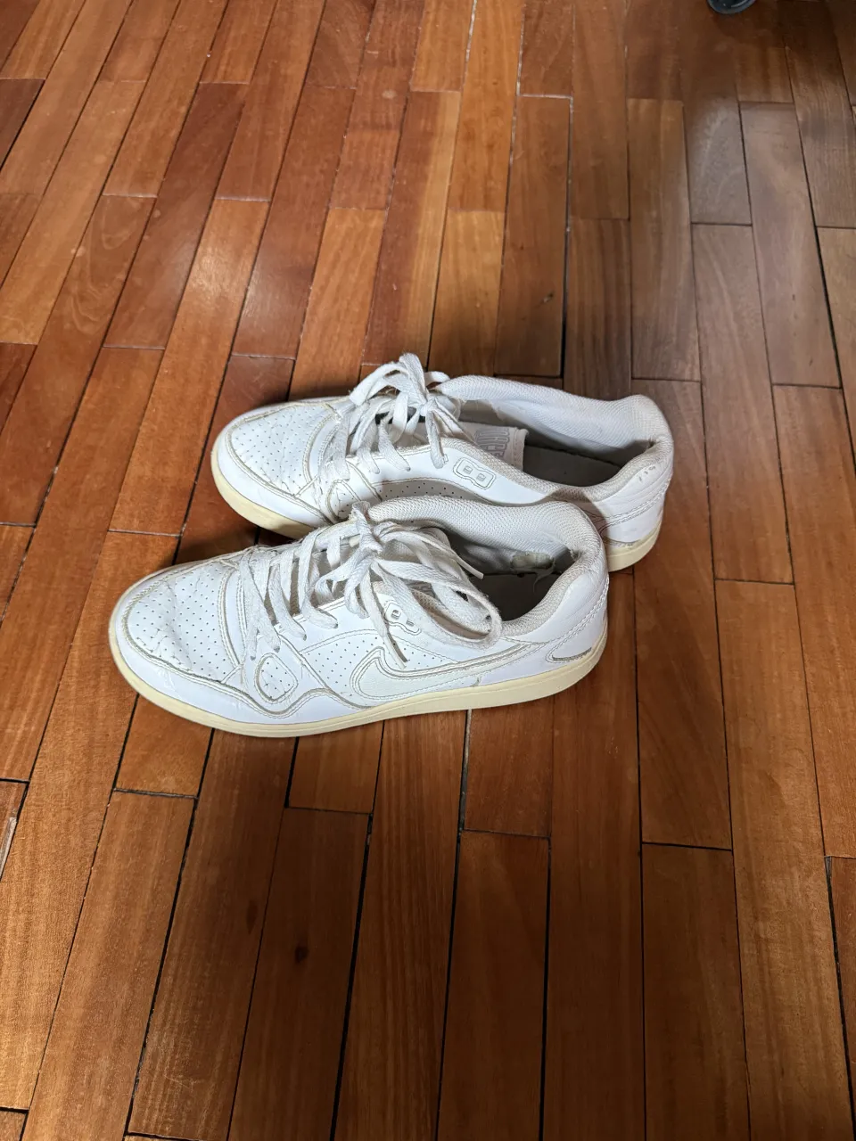 Zapatillas blancas de cuero con cordones. Tienen perforaciones en la punta y detalles de costuras. La suela es de goma color crema. En la lengüeta se lee 'FORCE'.