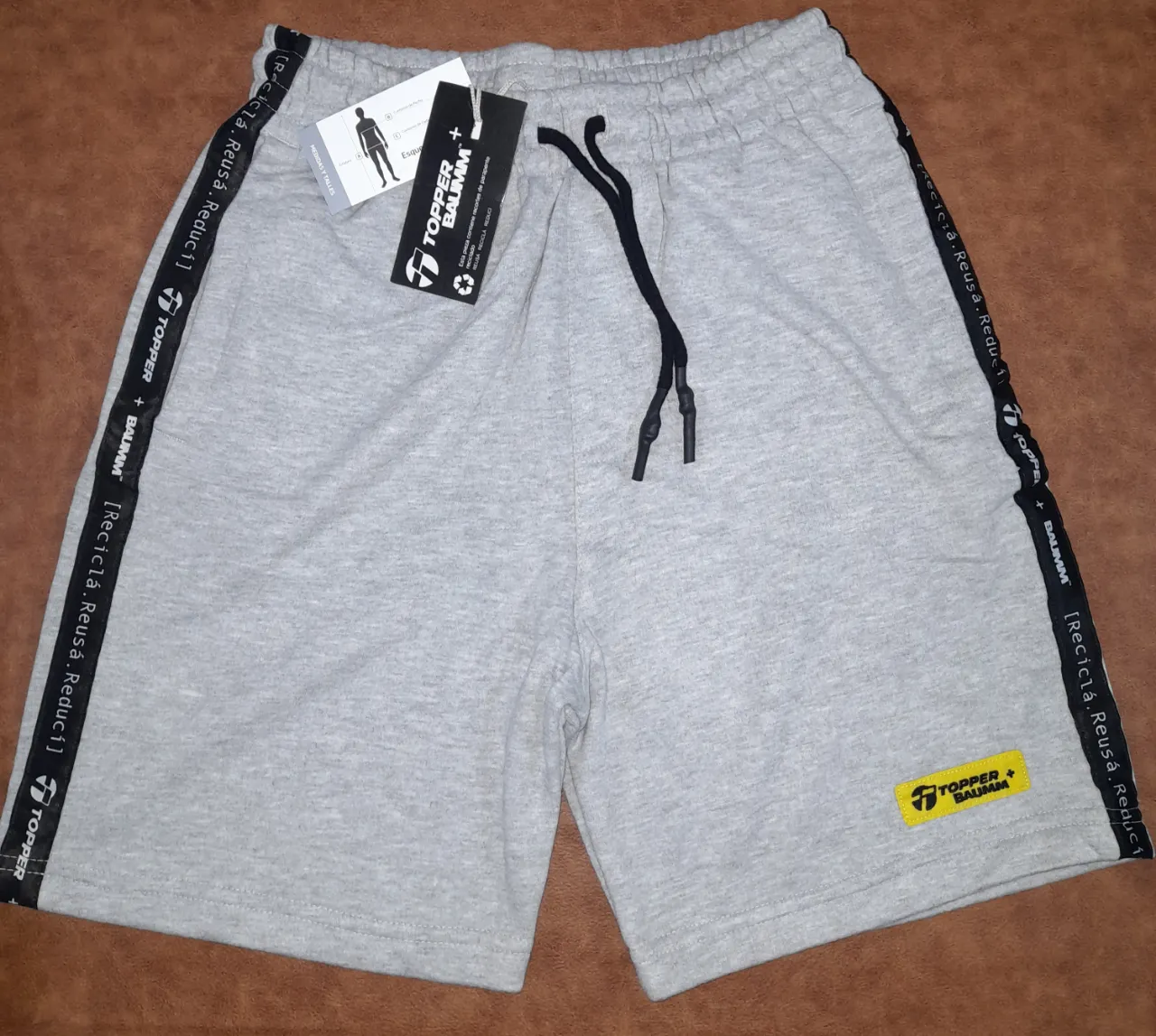 Short unisex Topper, de corte deportivo, color gris. Con detalles en negro en los laterales y el logo de la marca en la parte delantera. Ideal para actividades físicas o uso casual.