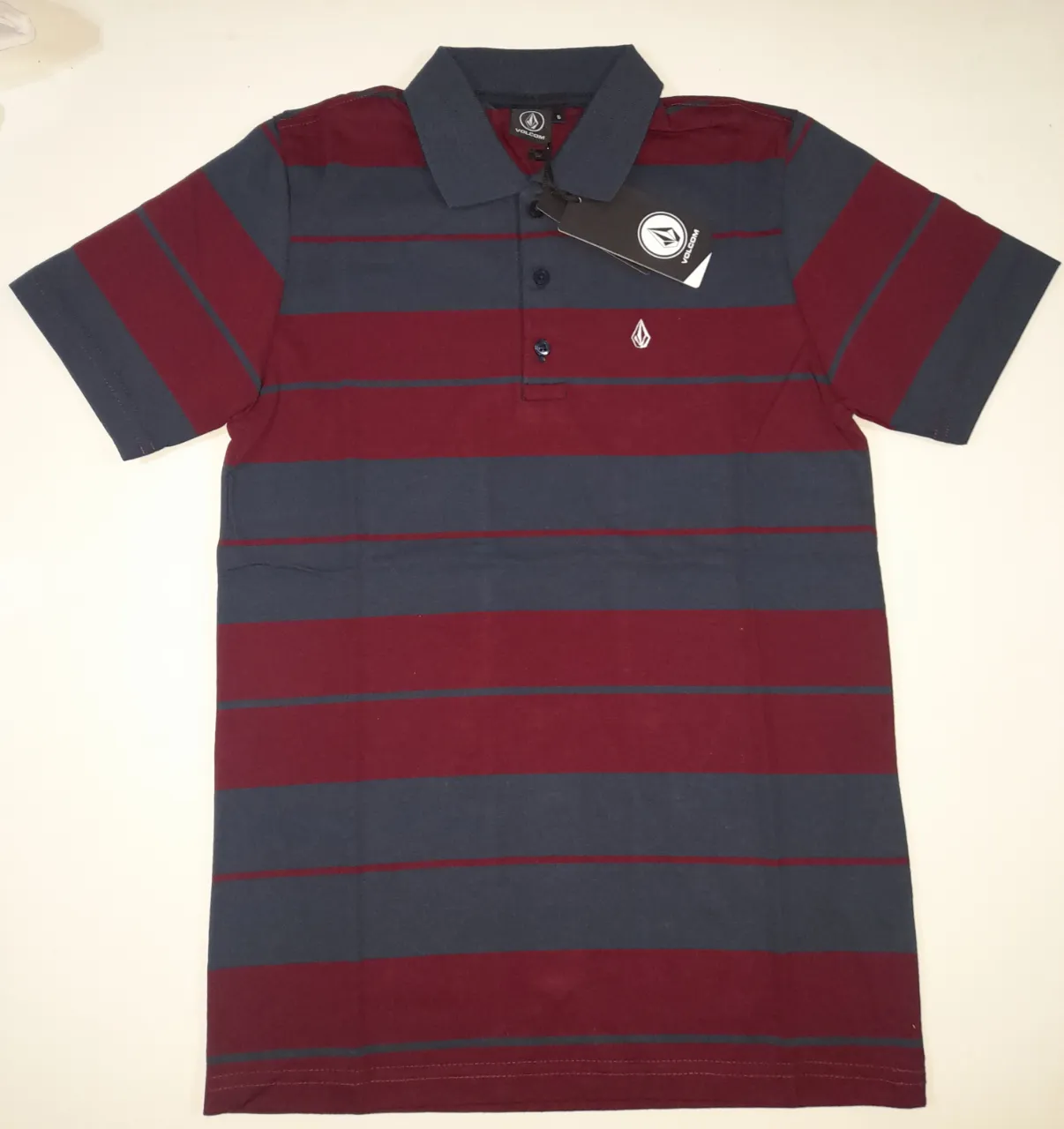 Remera polo a rayas horizontales en azul y bordo, con cuello y mangas en azul. Marca Volcom.