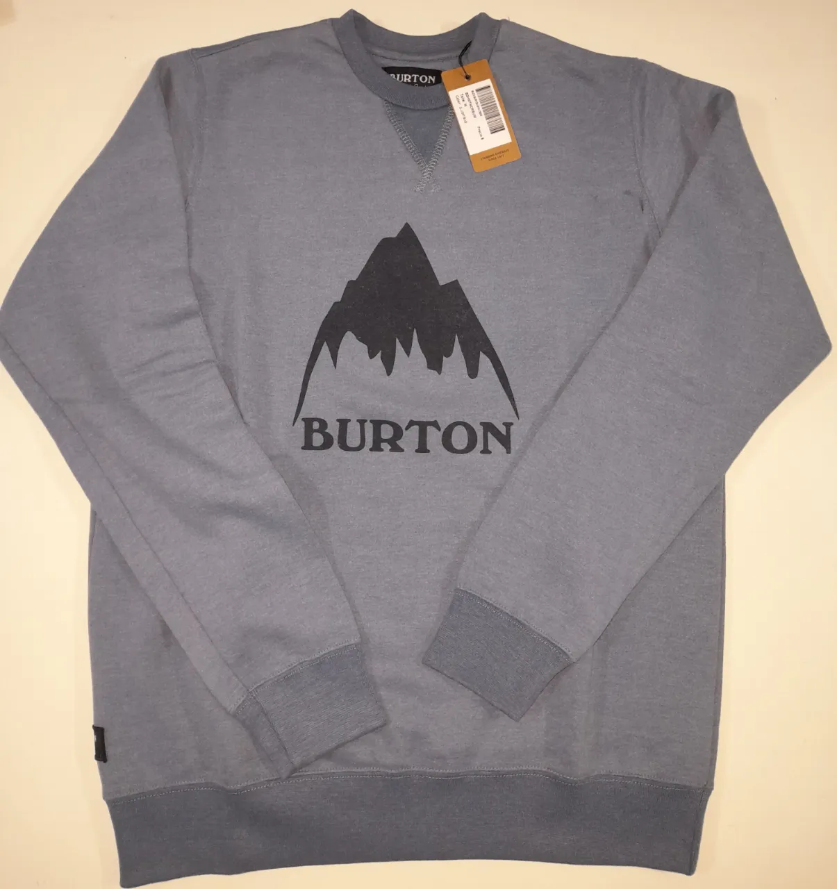 Buzo de cuello redondo de hombre, color azul con logo de montaña y la marca Burton en el frente..Frizado..El único defecto es una marchita negra bajo el hombro derecho (foto 6). Ideal para un look casual y cómodo. 