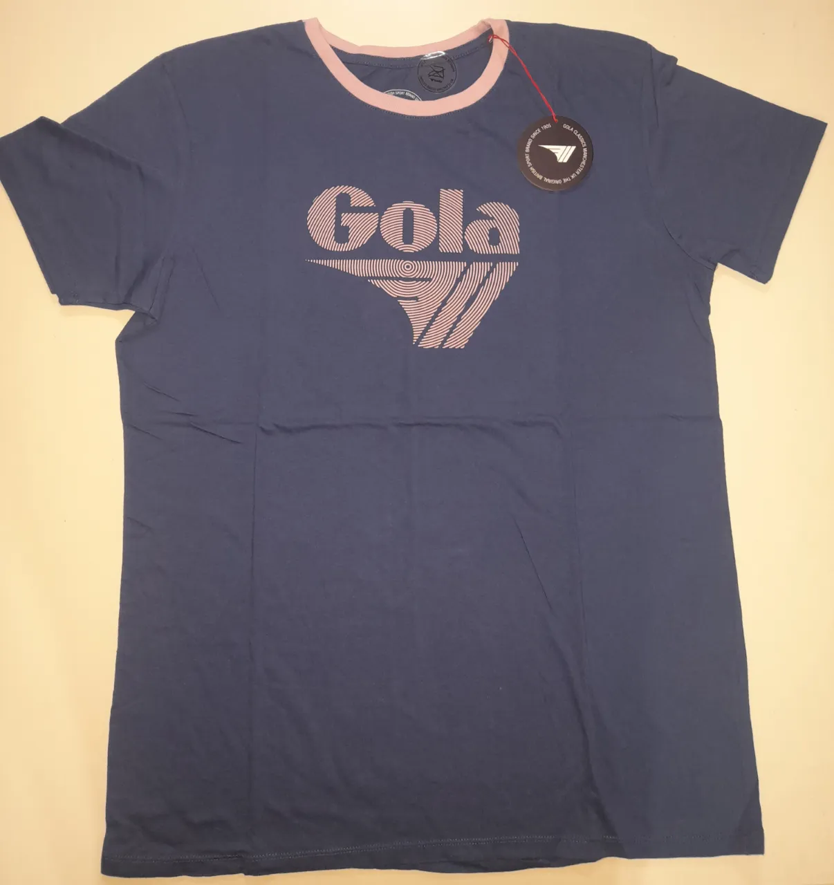 Remera Gola azul marino con cuello y detalles en rosa, ideal para un look casual y cómodo. Con el logo de la marca estampado en el frente. Unico detalle desteñido en la parte posterior de una manga. Foto 6. Talle M.
