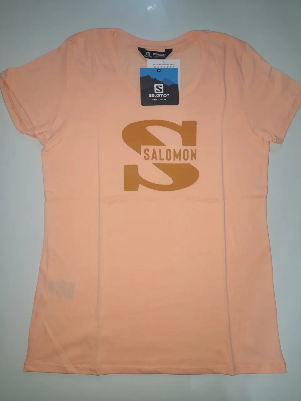 Remera deportiva de mujer, color naranja, con el logo de Salomon estampado en el frente. Ideal para actividades al aire libre.