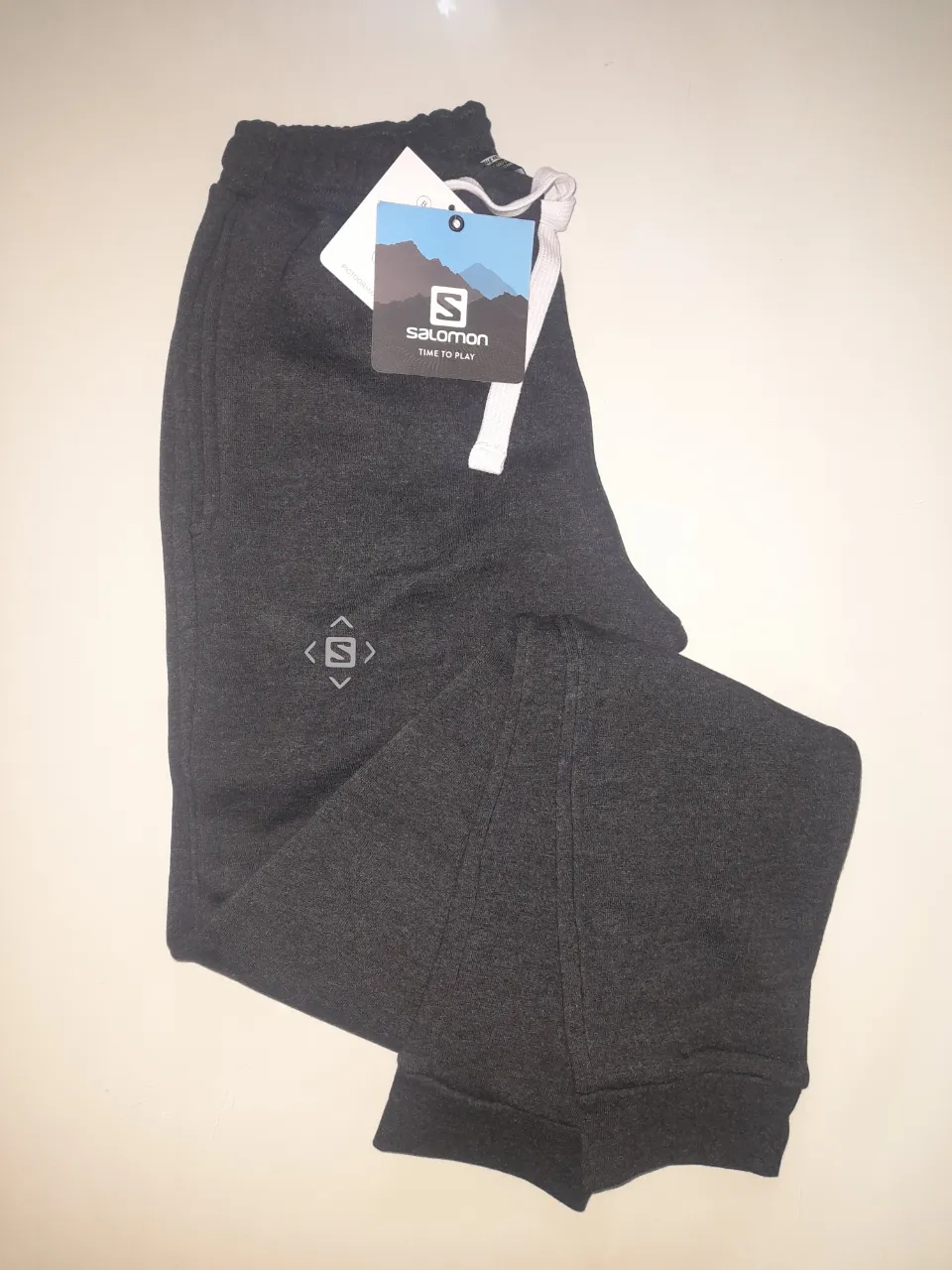 Pantalón deportivo de mujer Salomon, color gris oscuro, con logo de la marca. Ideal para actividades deportivas y uso diario. Talle XS.