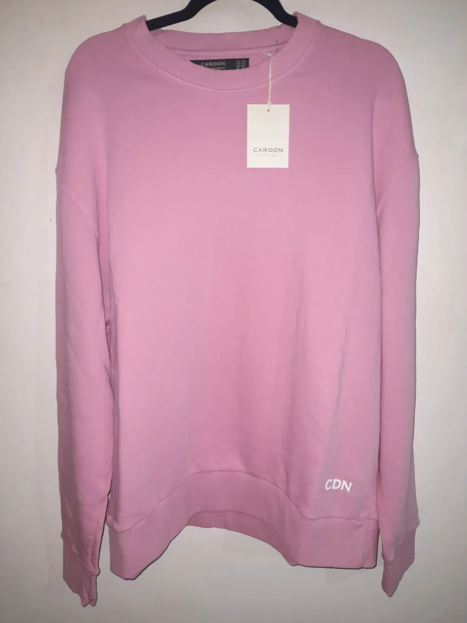 Buzo rosa de cuello redondo, ideal para un look casual y cómodo. Presenta un pequeño logo 'CDN' bordado en la parte inferior derecha. Perfecto para el día a día.