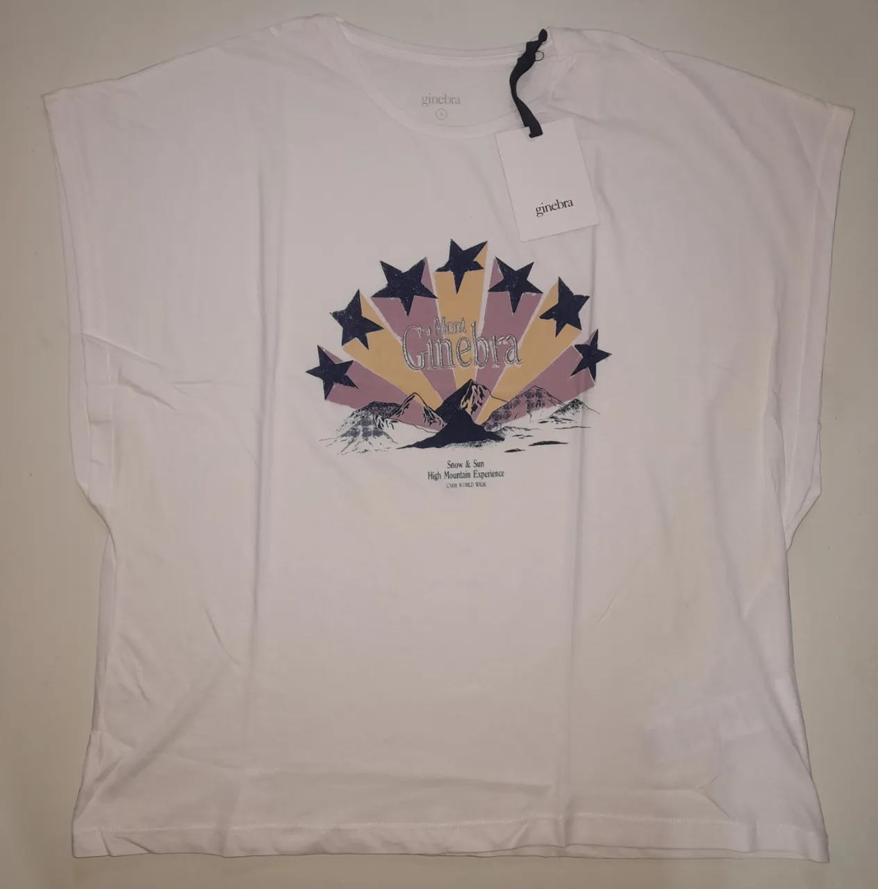 Remera blanca sin mangas  con estampado "Mont Ginebra" en el frente. Diseño con estrellas y montañas, ideal para un look casual y con estilo.