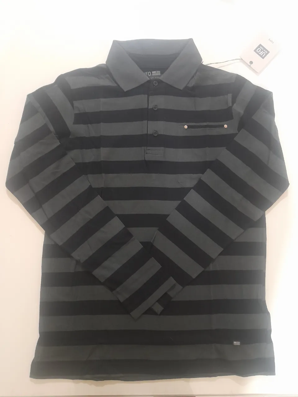 Remera manga larga a rayas grises y negras, con cuello polo y bolsillo en el pecho. Marca UFO.
