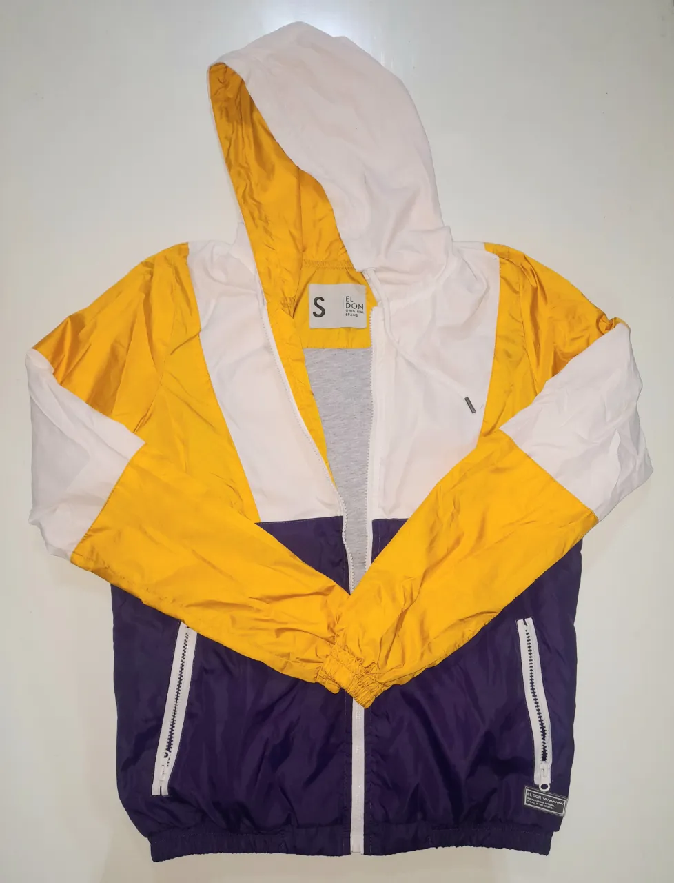 Campera rompevientos unisex, con capucha, combinada en amarillo, blanco y azul. Ideal para actividades deportivas o uso casual. Talle S. intacta..una marchita en la capucha y una en la.manga izquierda...