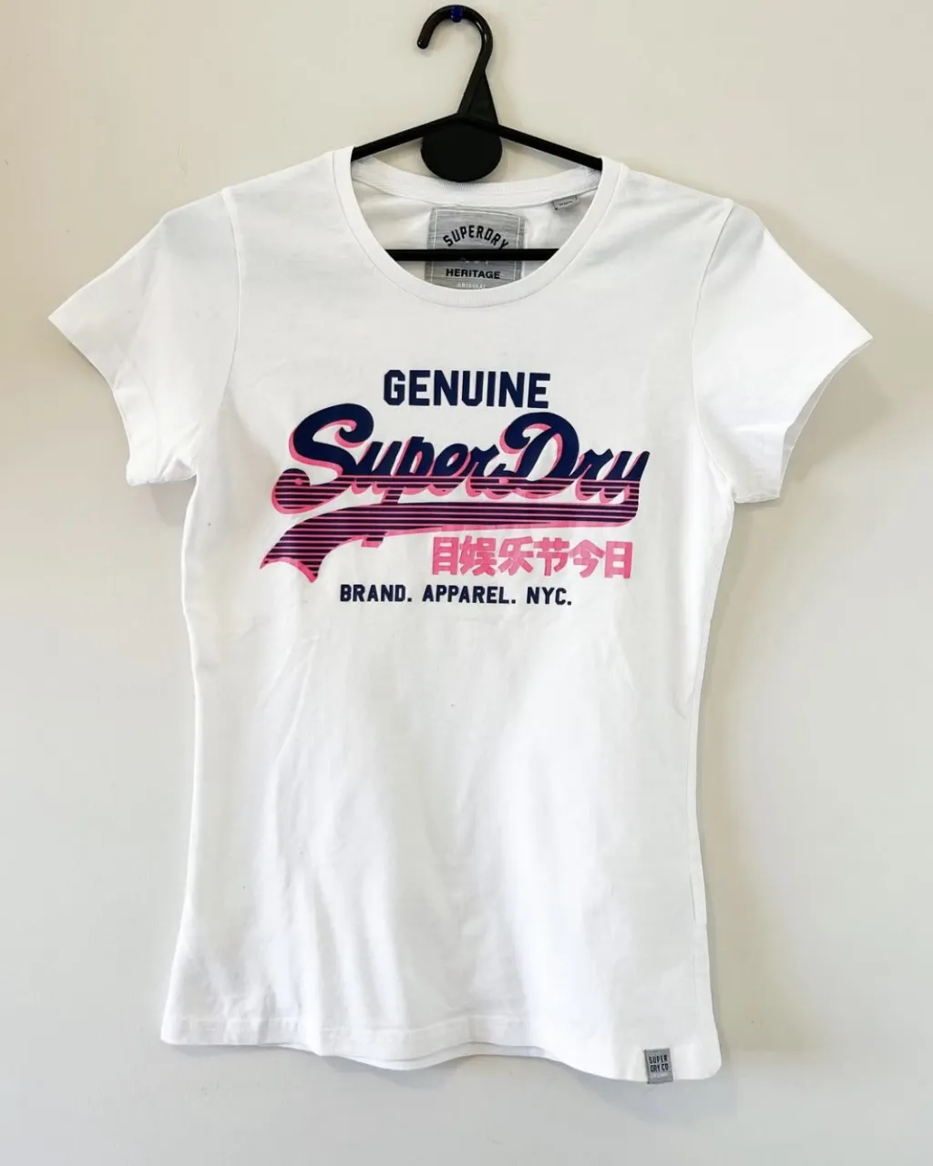 Remera blanca de manga corta con estampa "Super Dry" en degradé de rosa y azul. Cuello redondo. Ideal para un look casual y moderno.