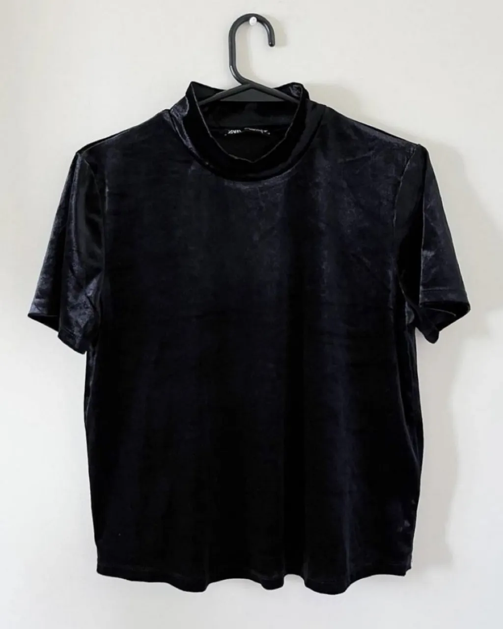 Remera negra de terciopelo con cuello alto y mangas cortas. Un básico elegante y versátil, ideal para complementar cualquier look. es de tela velvet