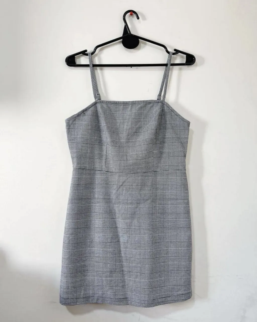 Vestido corto a cuadros grises, con tiras finas y escote cuadrado. Ideal para un look casual y moderno.