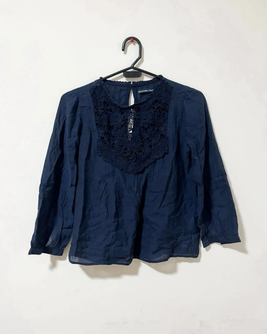 Blusa de manga larga azul marino con detalles de encaje en el cuello y la espalda. Un toque romántico y elegante para cualquier ocasión.