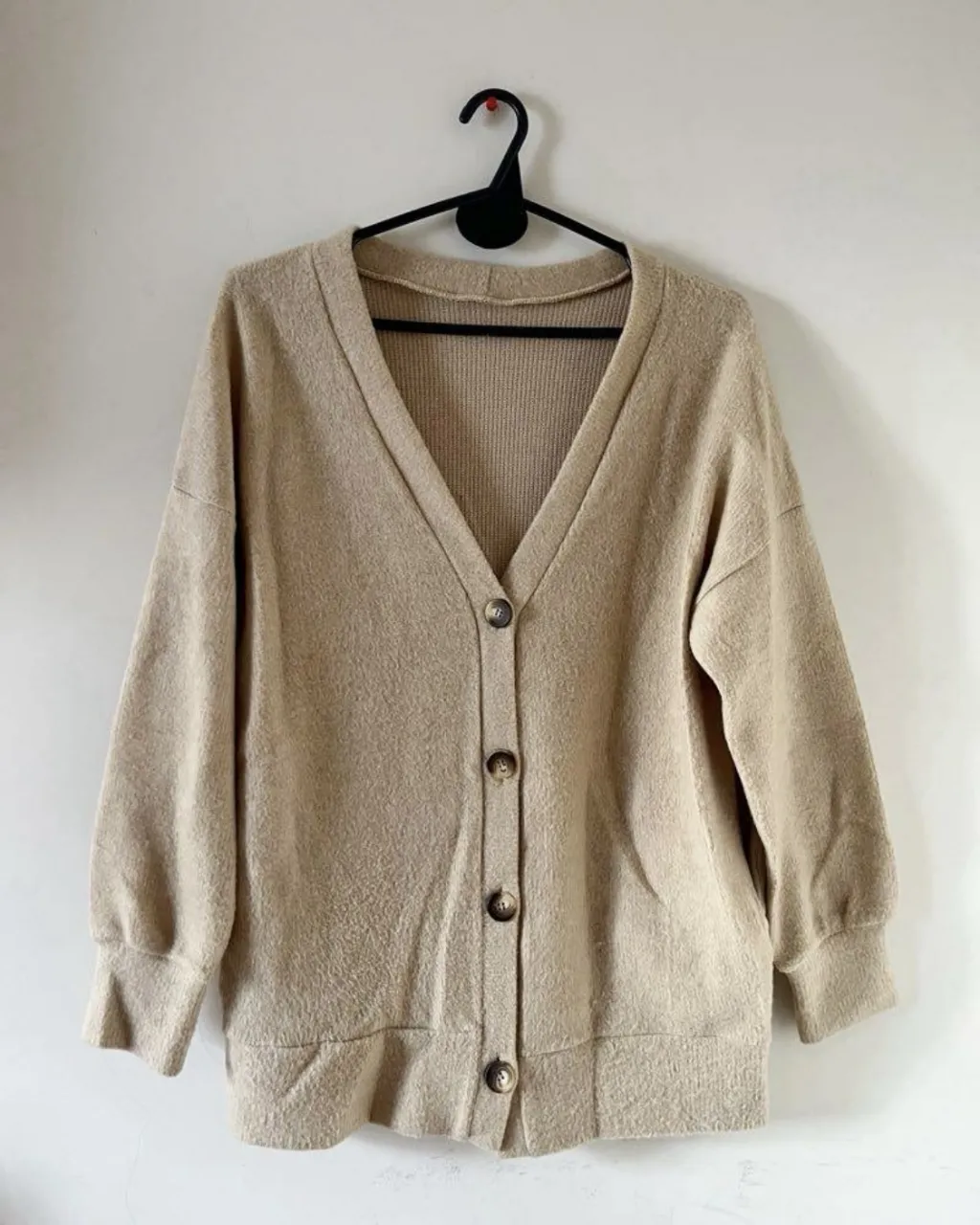 Cardigan de tejido suave en color beige, con botones al frente y escote en V. Un básico súper cómodo y versátil para sumar a tu guardarropa.