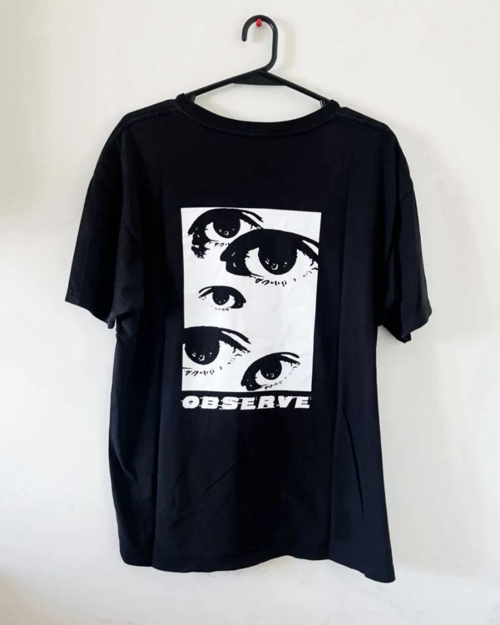 Remera negra oversize con estampa de ojos y la palabra "OBSERVE" en el frente. Un diseño único y llamativo para un look urbano.